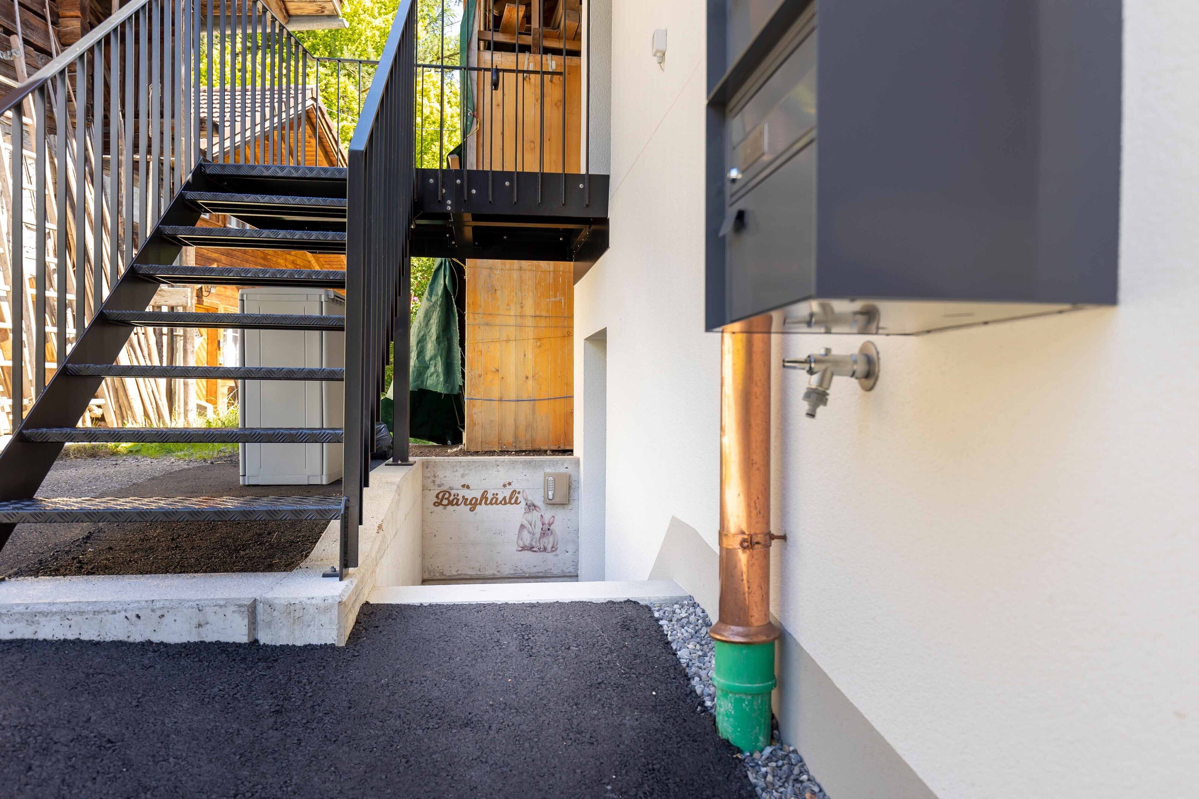 A staircase leading to a wooden deck, a metal gate, and a wall-mounted water spigot.