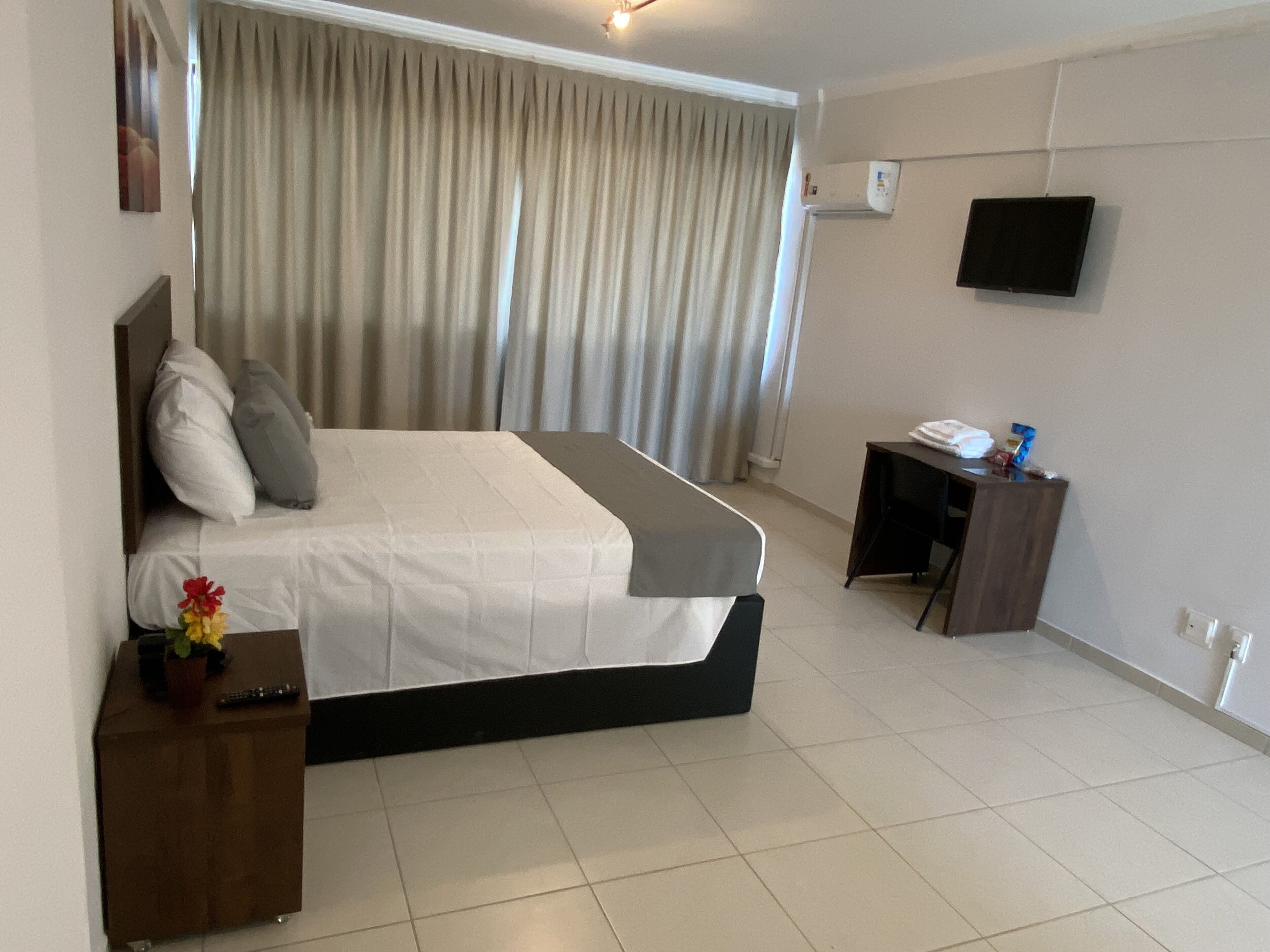 A hotel room with a bed, a desk, a TV, and a curtain.