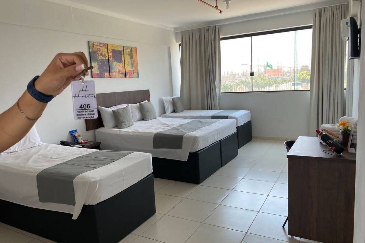 A hotel room with two beds, a desk, a chair, a window with curtains, a painting on the wall, and a sign with room number 406.