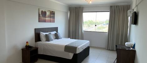 A bedroom with a bed, a nightstand, a dresser, a window with curtains, and a ceiling light fixture.