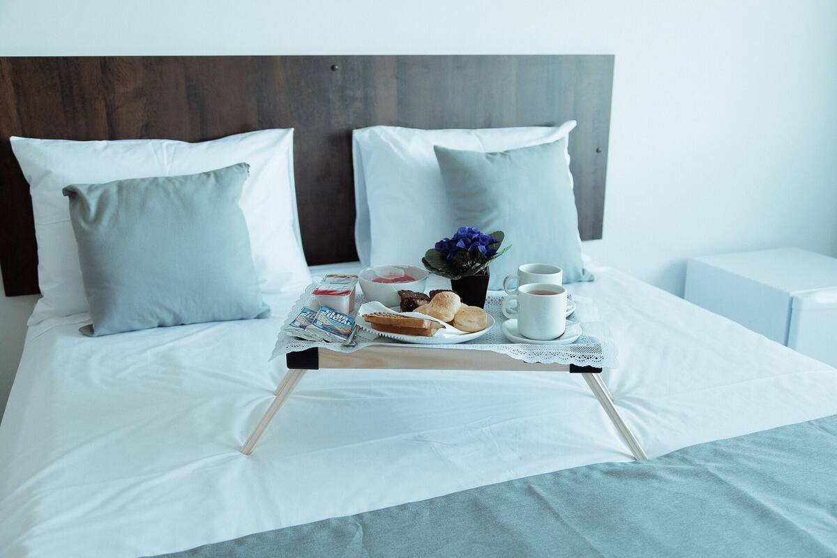 A neatly made bed with pillows, a tray with breakfast items, and a cup of coffee.