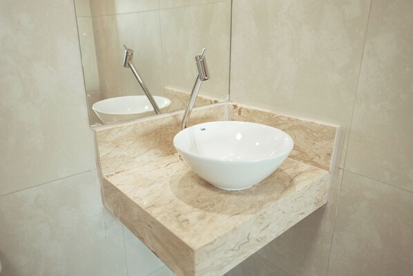 Un baño con lavamanos blanco, espejo y encimera de mármol.