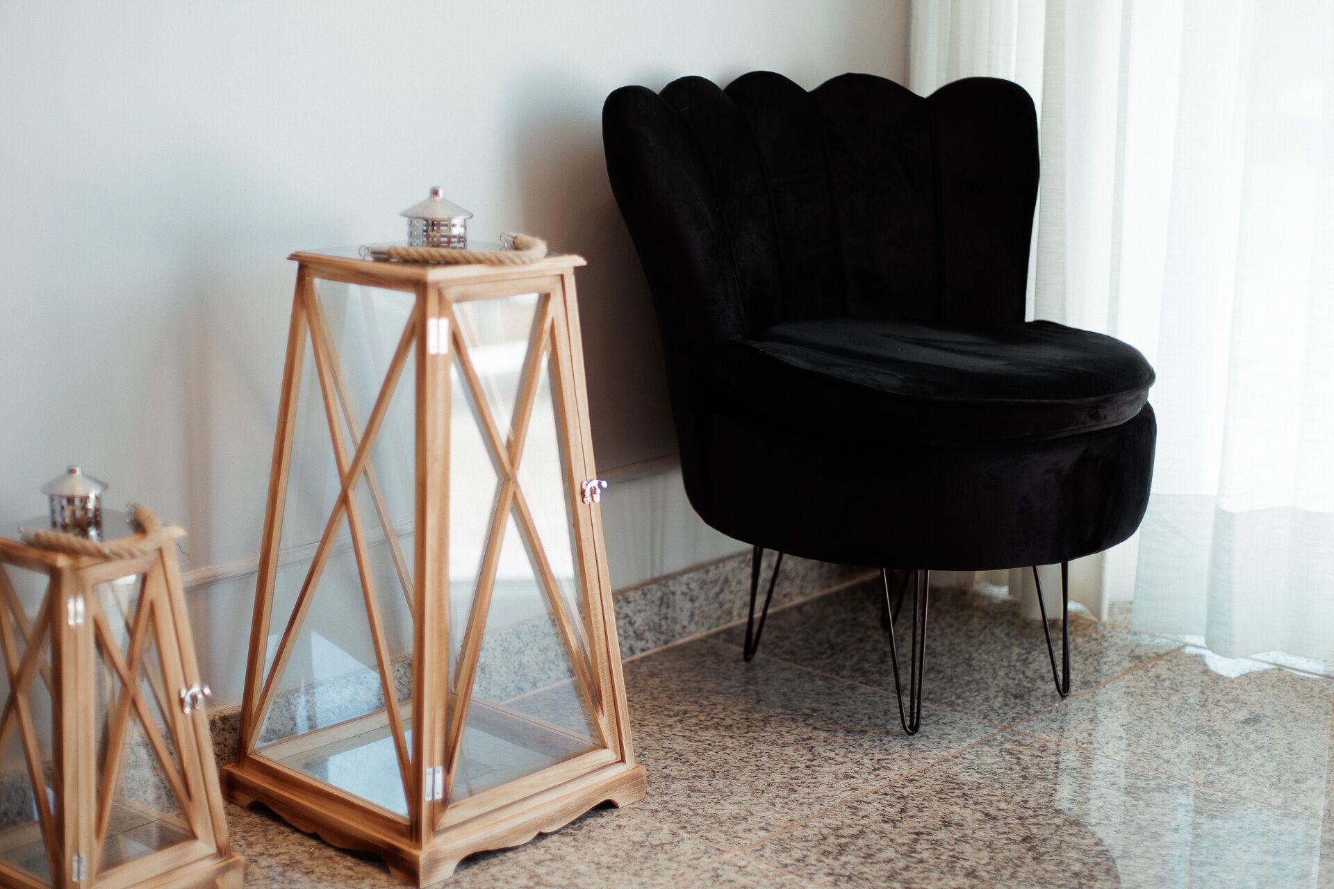 Una habitación con una silla negra, una mesita de noche de madera con paneles de vidrio y un pequeño farol.