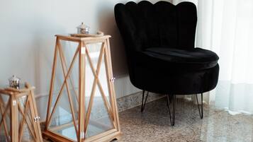Una habitación con una silla negra, una mesita de noche de madera con paneles de vidrio y un pequeño farol.