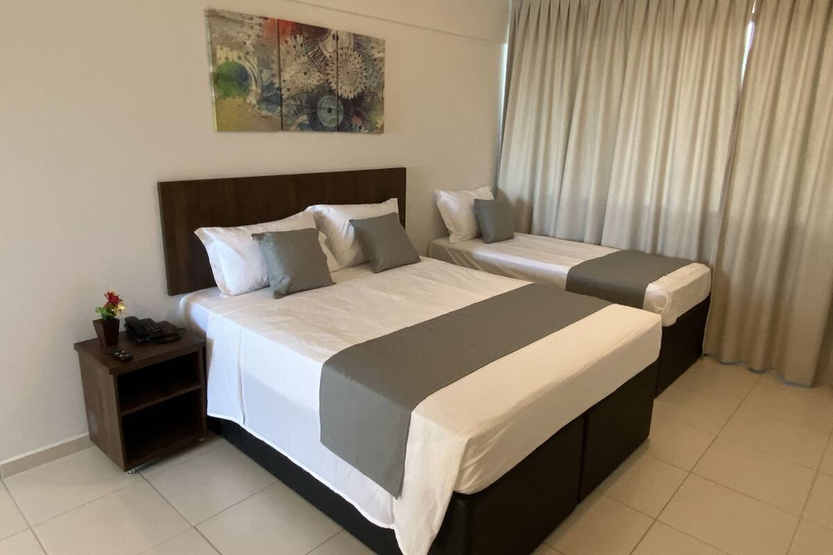 A hotel room with two beds, a nightstand, a painting, and a window with curtains.