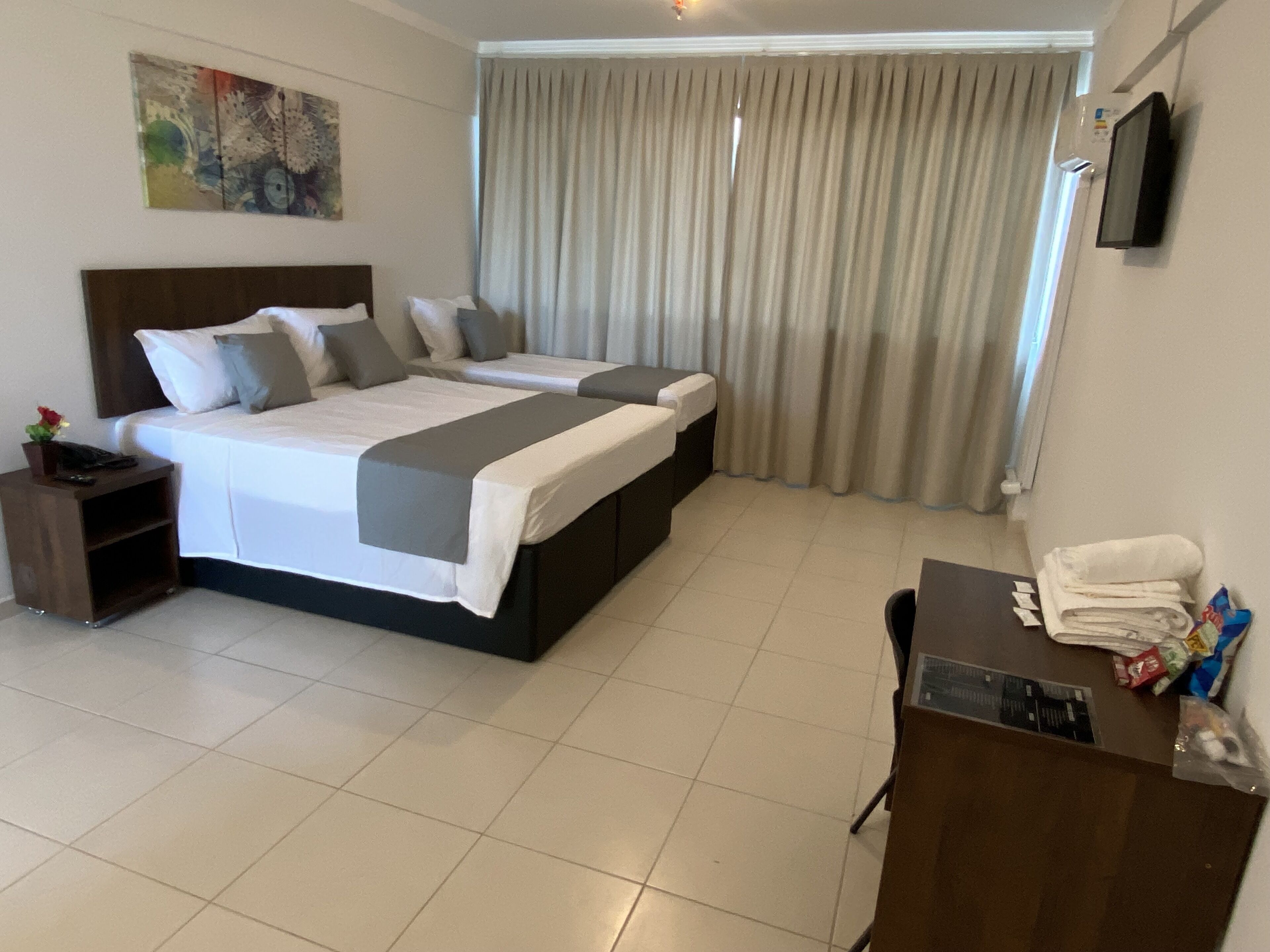 A hotel room with a large bed, a desk, and a TV on the wall.