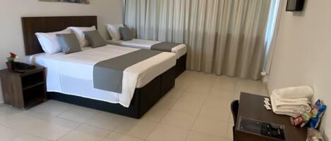 A hotel room with a large bed, a desk, and a TV on the wall.