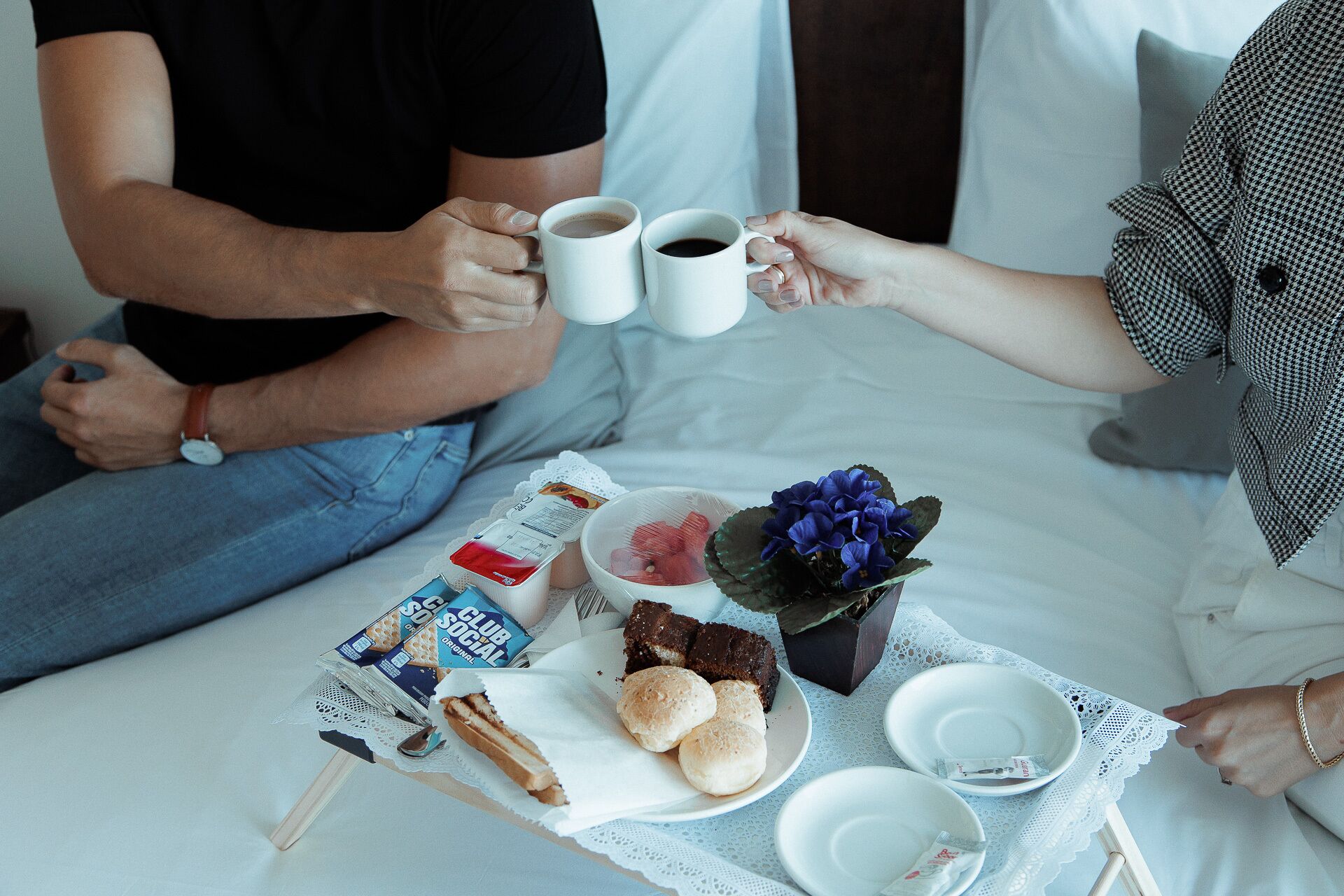 Una bandeja de desayuno con pasteles, un pastel y un ramo de flores sobre una cama.