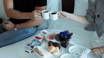 A breakfast tray with pastries, a cake, and a bouquet of flowers on a bed.