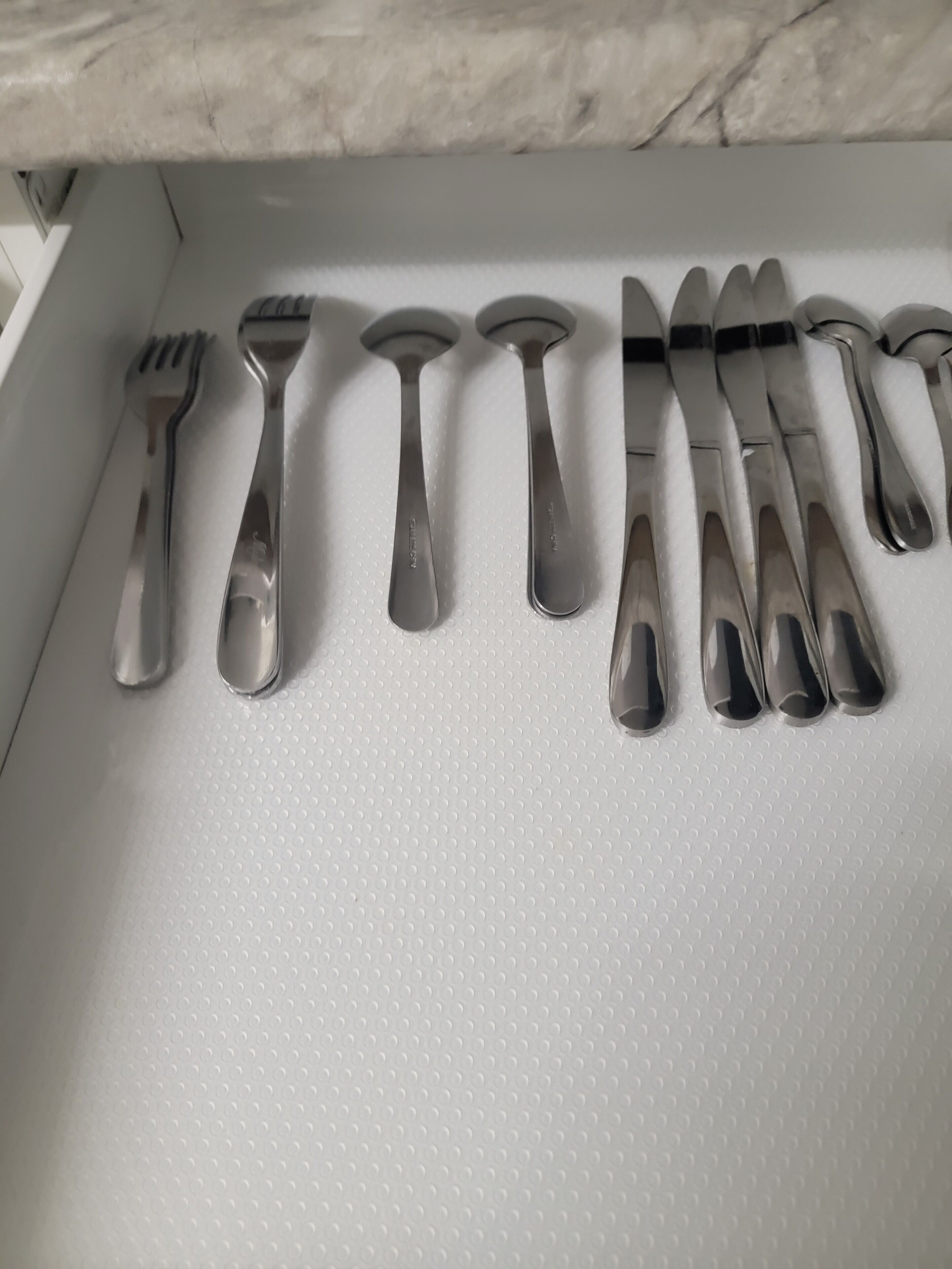 A drawer containing a set of stainless steel cutlery including forks, knives, and spoons.
