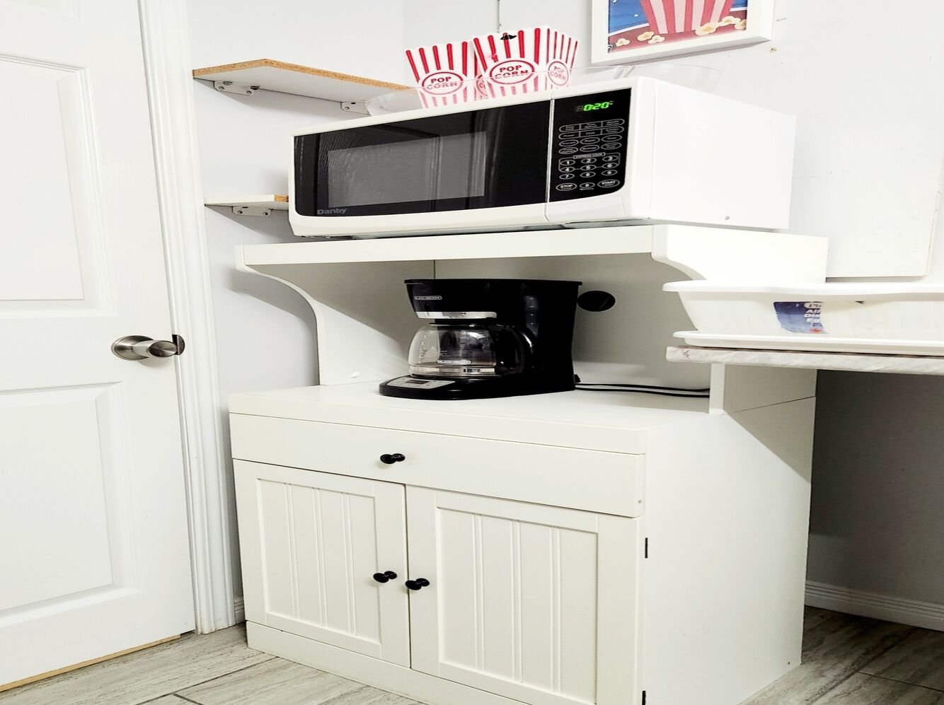 A compact kitchenette with a microwave, coffee maker, and storage cabinets.