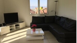 A living room with a black sofa, a white coffee table with a flower, a TV on a white stand, and a view of a person working outside.