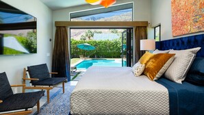 Ein modernes Schlafzimmer mit einem großen Bett, Blick auf einen Swimmingpool und einer hellen Pendelleuchte.