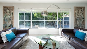 Ein modernes Wohnzimmer mit Ledersofas, einem Glastisch und großen Fenstern mit Blick auf einen Garten.