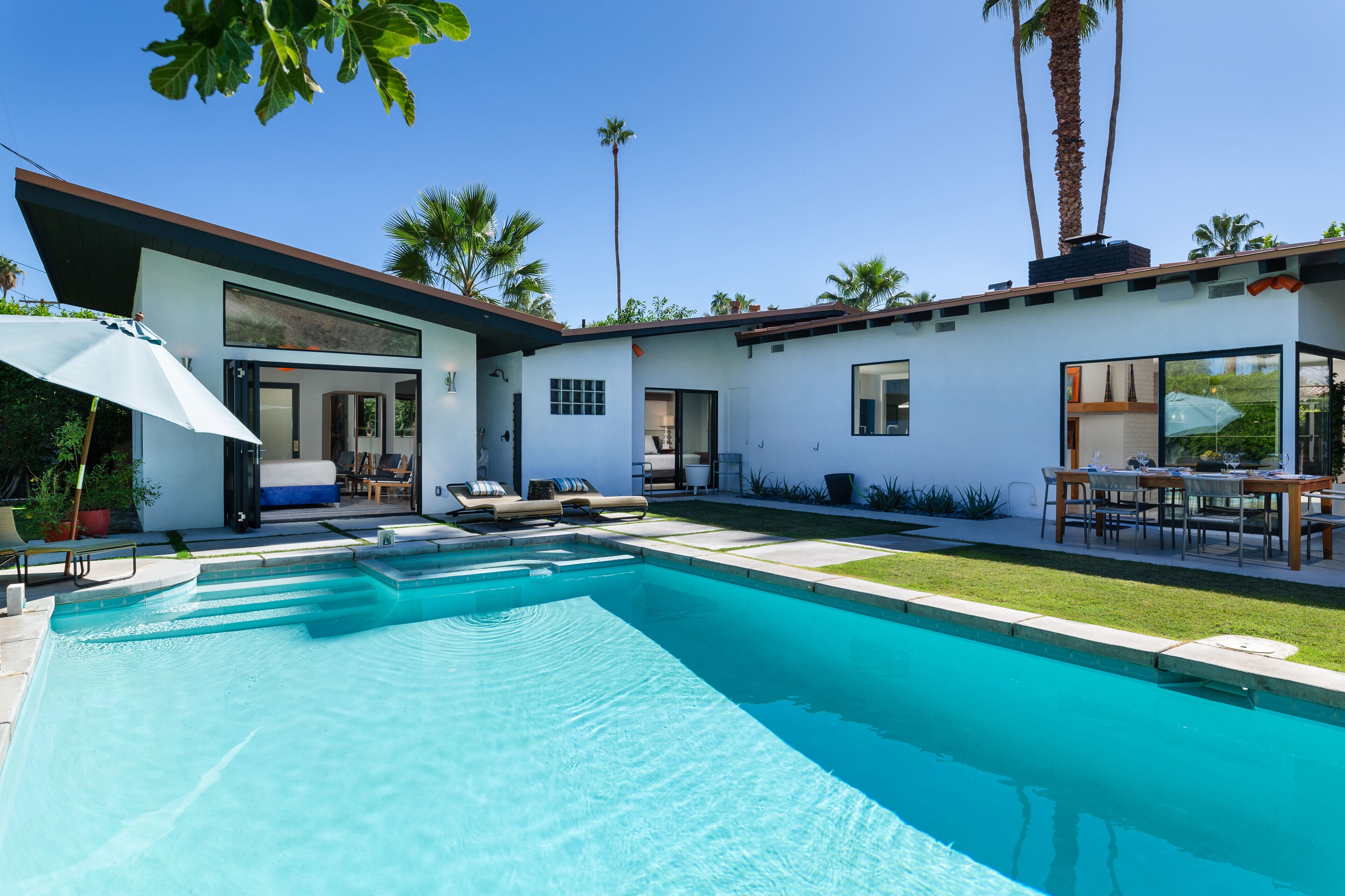 Une maison moderne dotée d’une piscine, de mobilier d’extérieur et de palmiers.