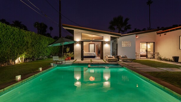 Ein modernes Haus mit Swimmingpool, einer Terrasse mit Gartenmöbeln und einem gut beleuchteten Innenraum.
