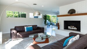 Ein modernes Wohnzimmer mit einer braunen Ledersofa, einem Glastisch und einem Kamin mit weißen Ziegelsteinen.