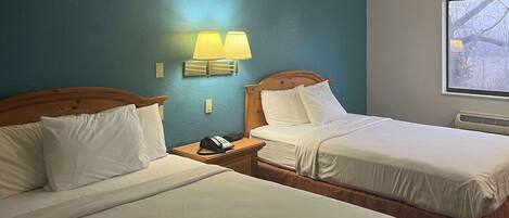 A hotel room with two beds, a nightstand with a phone, and a window with a view of trees.