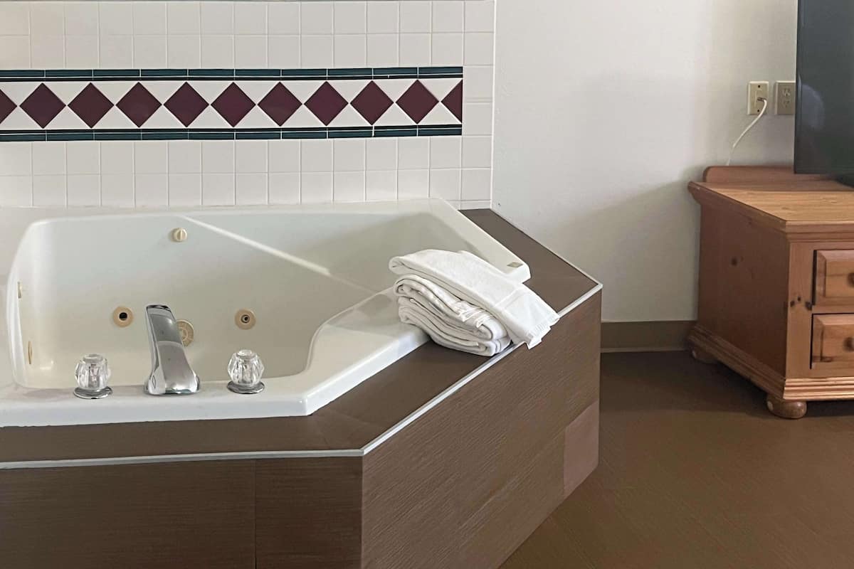 A bathroom with a large bathtub, a wooden cabinet, and a tiled wall with a decorative border.