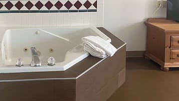 Une salle de bain avec une grande baignoire, un meuble en bois et un mur carrelé agrémenté d’une bordure décorative.
