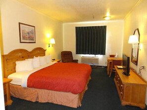A hotel room with a large bed, a desk with a computer, a chair, and a window with curtains.