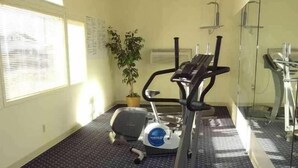 A gym with exercise equipment, a potted plant, and a window with blinds. - Motel 6 Portland, IN (Portland)