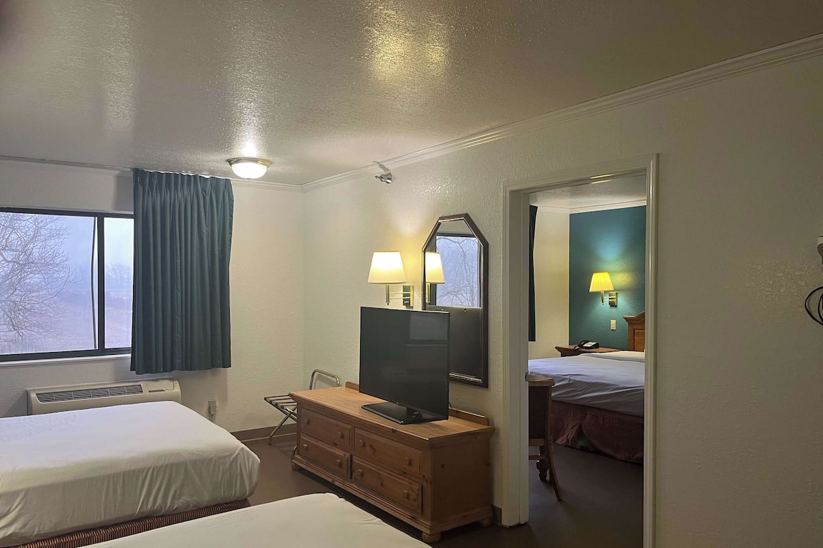 A hotel room with two beds, a desk with a TV, a dresser, and a window with curtains.