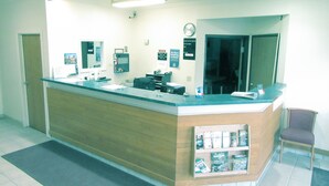 A reception desk with a wooden counter, a clock, and a no-smoking sign. - Motel 6 Portland, IN (Portland)