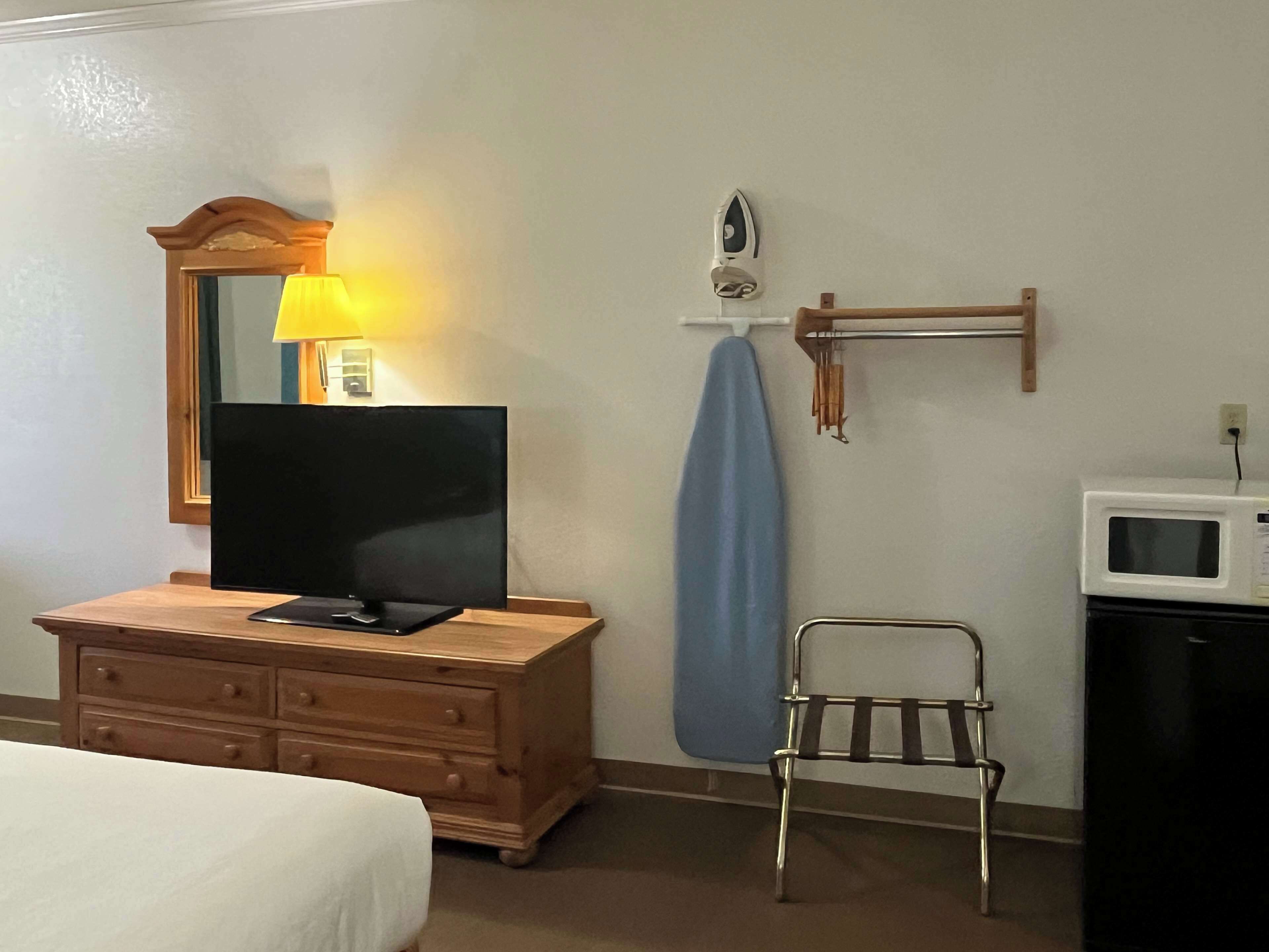 Une chambre d’hôtel avec une commode en bois, un téléviseur à écran plat, un four à micro-ondes et une petite chaise en métal.