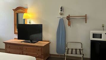 Une chambre d’hôtel avec une commode en bois, un téléviseur à écran plat, un four à micro-ondes et une petite chaise en métal.
