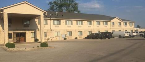 A multi-story motel with a covered entrance, several windows, and a parking lot with vehicles.