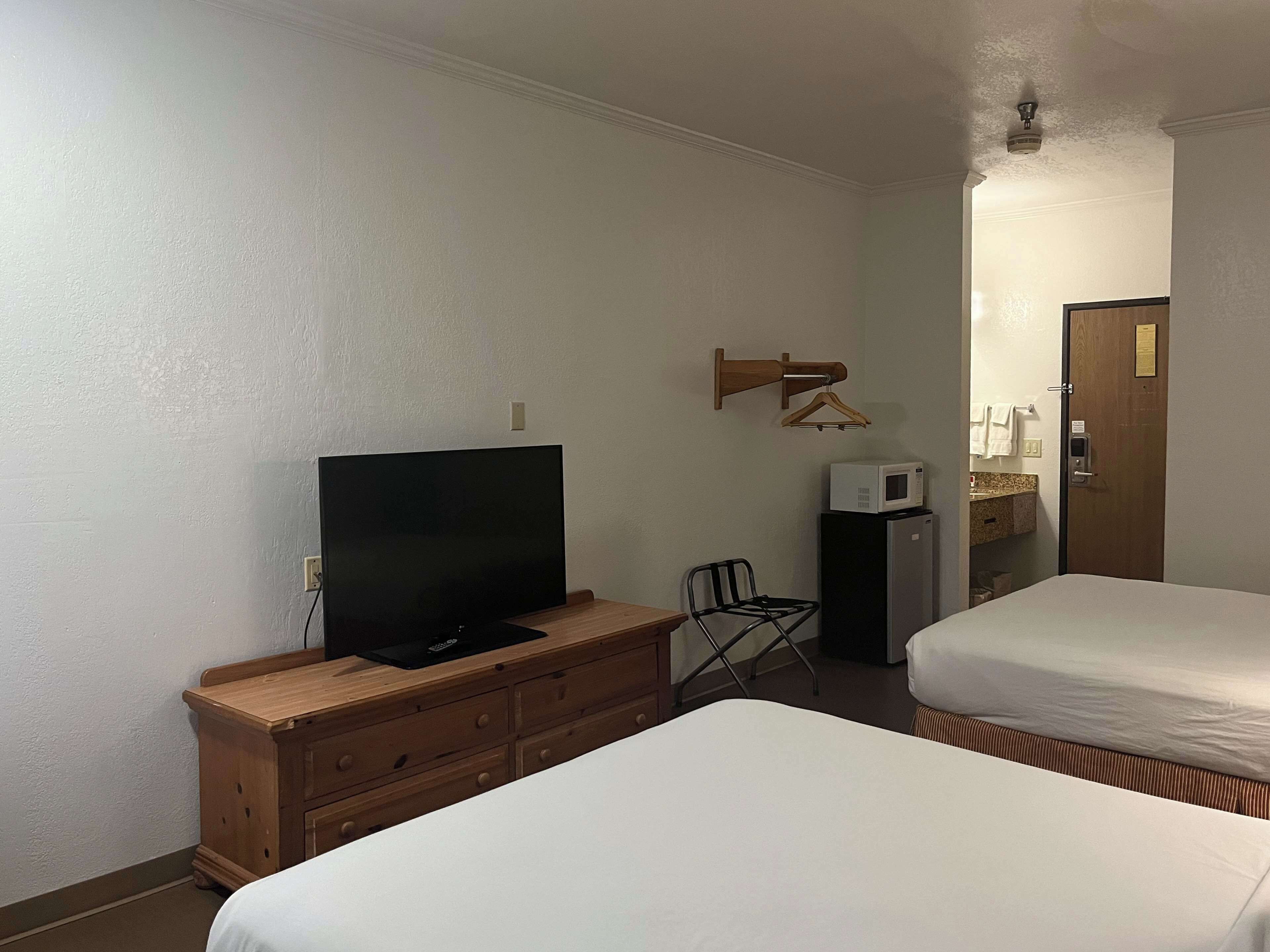 A hotel room with two beds, a TV on a wooden dresser, a microwave, and a wooden coat rack.