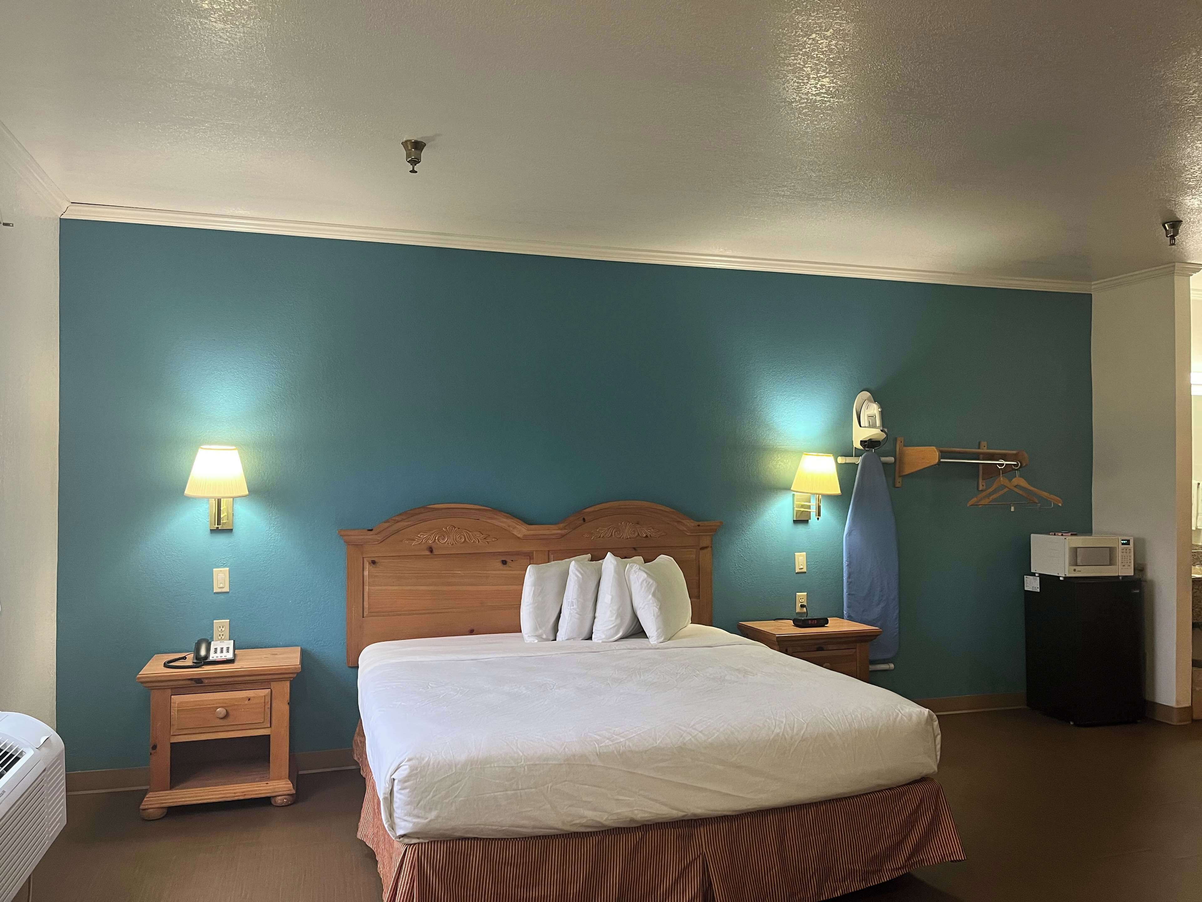 A hotel room with a large bed, two bedside tables with lamps, a wooden headboard, and a wall-mounted ironing board.