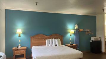 A hotel room with a large bed, two bedside tables with lamps, a wooden headboard, and a wall-mounted ironing board.
