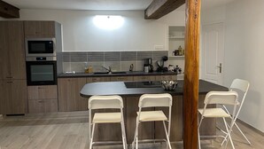 Une cuisine moderne dotée d’appareils électroménagers intégrés, d’un îlot central avec des tabourets de bar et d’un plafond avec poutres apparentes en bois.
