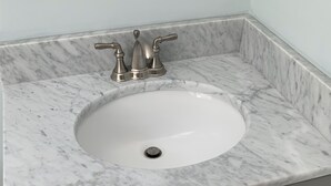 Une salle de bain avec un lavabo en marbre, des meubles gris et des carreaux hexagonaux.