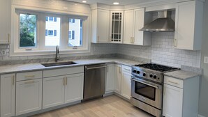Une cuisine moderne avec des meubles blancs, une cuisinière en acier inoxydable et une fenêtre donnant sur une maison.