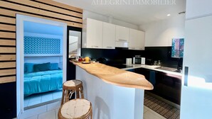 A modern kitchen with white cabinets, a wooden countertop, and a built-in stove. There is a small seating area with a blue bed and two wicker stools. - Beautiful villa 10 min walk from Ile Rousse (monticello)