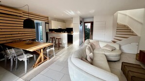 A modern living room with a white sofa, wooden dining table, and a kitchen in the background. - Beautiful villa 10 min walk from Ile Rousse (monticello)