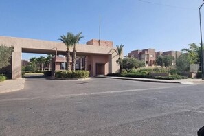 A building entrance with a large archway, palm trees, and a clear sky. - Luxury Apartment - Prestigia Marrakech Golf City (Marrakech)