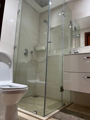 A modern bathroom with a glass-enclosed shower, a toilet, and a vanity with a mirror. - Luxury Apartment - Prestigia Marrakech Golf City (Marrakech)