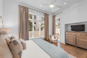 Een slaapkamer met een groot bed, een televisie, een dressoir en een raam met gordijnen.