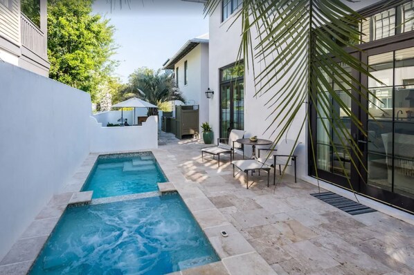 Een modern buitenzwembad met een jacuzzi, zitplaatsen en een glazen ruimte.