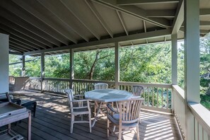Een overdekt terras buiten met een tafel en stoelen, omgeven door een houten balustrade en bomen op de achtergrond.