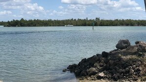Un lago tranquilo con cielo despejado, una lancha en el agua y una orilla rocosa con una palmera.