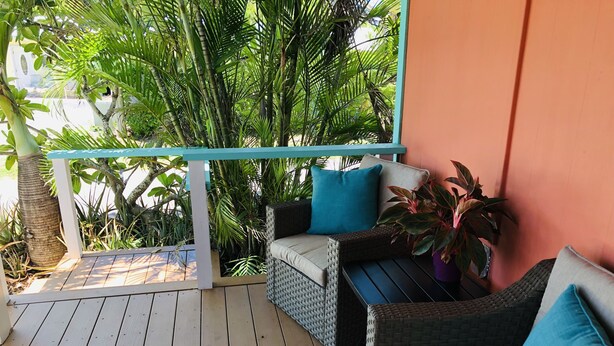 Terraza de madera con mobiliario de mimbre y vista a la vegetación exuberante.