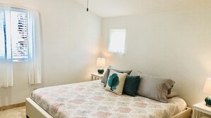 Un dormitorio con cama, mesita de noche, lámpara y ventana con cortinas.