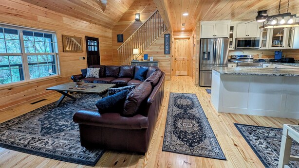 L’intérieur chaleureux d’un chalet, avec un revêtement mural en bois, un canapé en cuir, une table à manger et un coin cuisine.