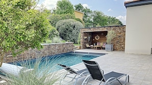 A swimming pool with lounge chairs, a stone wall, and a patio area with seating.