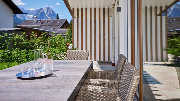 A patio with a table and wicker furniture, overlooking a mountain landscape. - Beary - modern ground floor flat in best location (Garmisch-Partenkirchen)